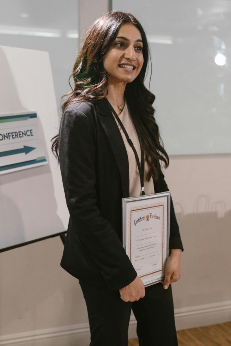 Smiling woman in business attire holding a certificate at a professional event indoors.